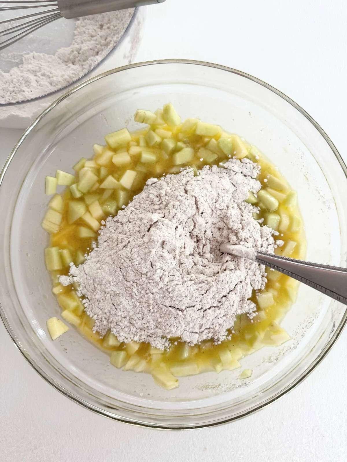 طرز تهیه کیک سیب: هم زدن آرد در مایه کیک میان وعده سیب.