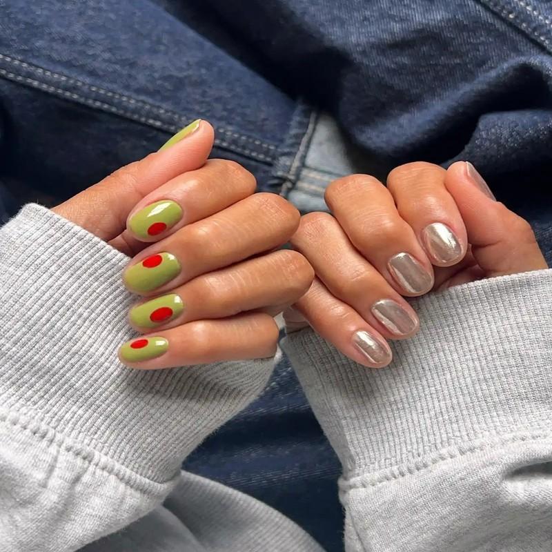 ایده ناخن زیتونی: Hands with manicure one with green and red nail art and the other with a metallic finish sweater sleeves and denim background