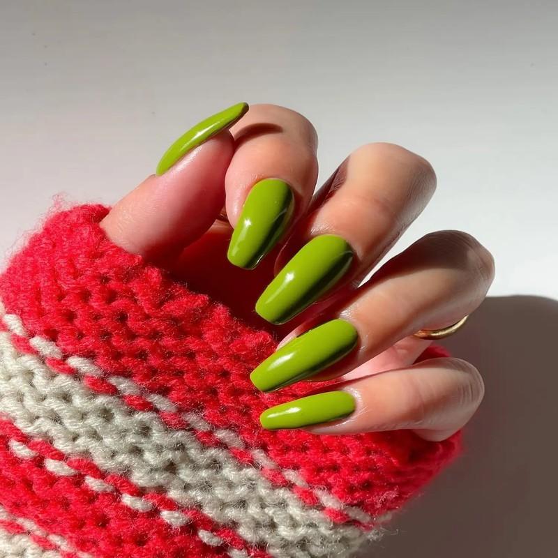 ایده ناخن زیتونی: A hand with long green manicured nails shown against a striped knit fabric background