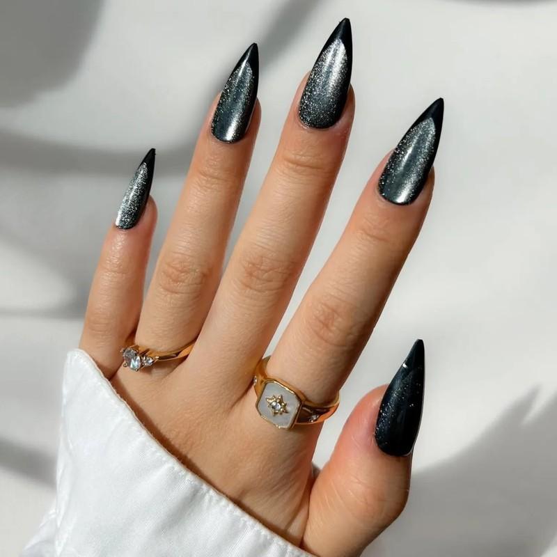 A hand with black and graphite velvet pointed nails and gold rings positioned against a neutral background - مدل ناخن مخملی
