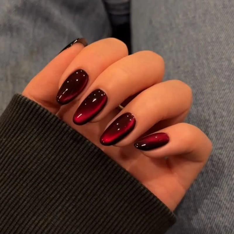 Hand showcasing manicured nails in a shiny oxblood cat eye design - مدل ناخن مخملی