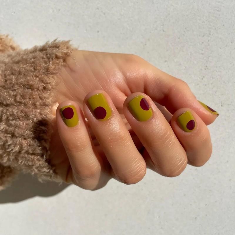ایده ناخن زیتونی: A hand showcasing manicured nails with a modern design featuring a yellow base with red circular accents on each nail