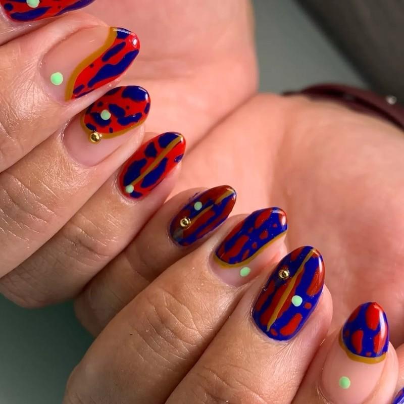 Closeup of manicured nails with bold abstract designs featuring high contrast red and blue patterns and small decorative elements, مدل ناخن کوتاه پاییزی انتزاعی