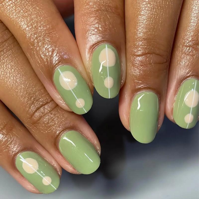A closeup of hands with green nail polish and dotted designs on the nails, مدل ناخن کوتاه پاییزی ماچا جو دوسر