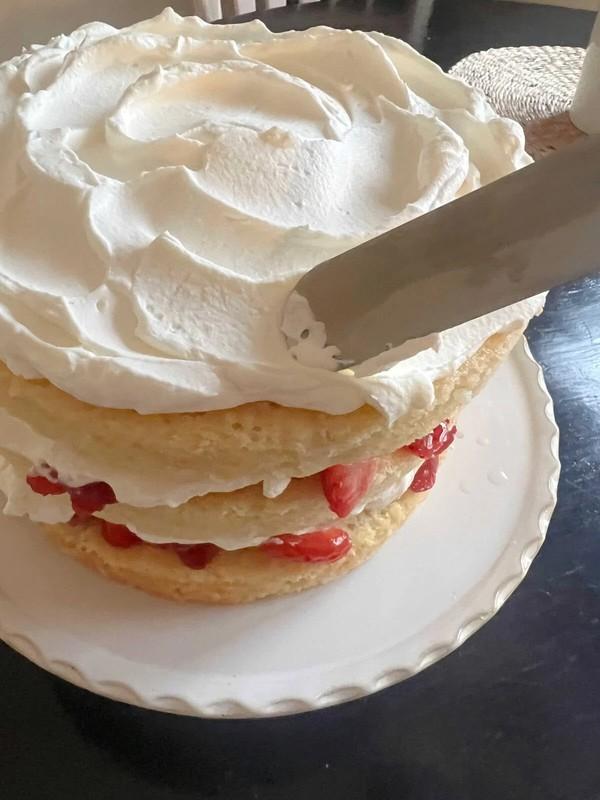 پخش کردن خامه فرم گرفته روی کیک - طرز تهیه کیک توت فرنگی خامه ای.