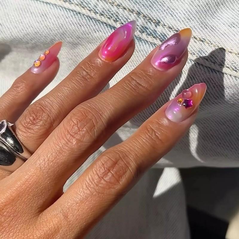 دستی با ناخن های بادامی بلند با طرح های ژل سه بعدی تصادفی، لاک پایه ابروبادی و فینیش ناخن کروم ملایم.